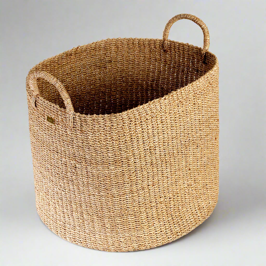 Camille Round Basket Hamper made from 100% natural plant fiber, featuring a beautifully woven design that adds rustic charm and eco-friendly storage to any room. Ideal for organizing laundry, toys, throw pillows, and bath essentials, while also enhancing home decor with indoor plants. Care instructions recommend avoiding prolonged water exposure and using spot cleaning for maintenance.